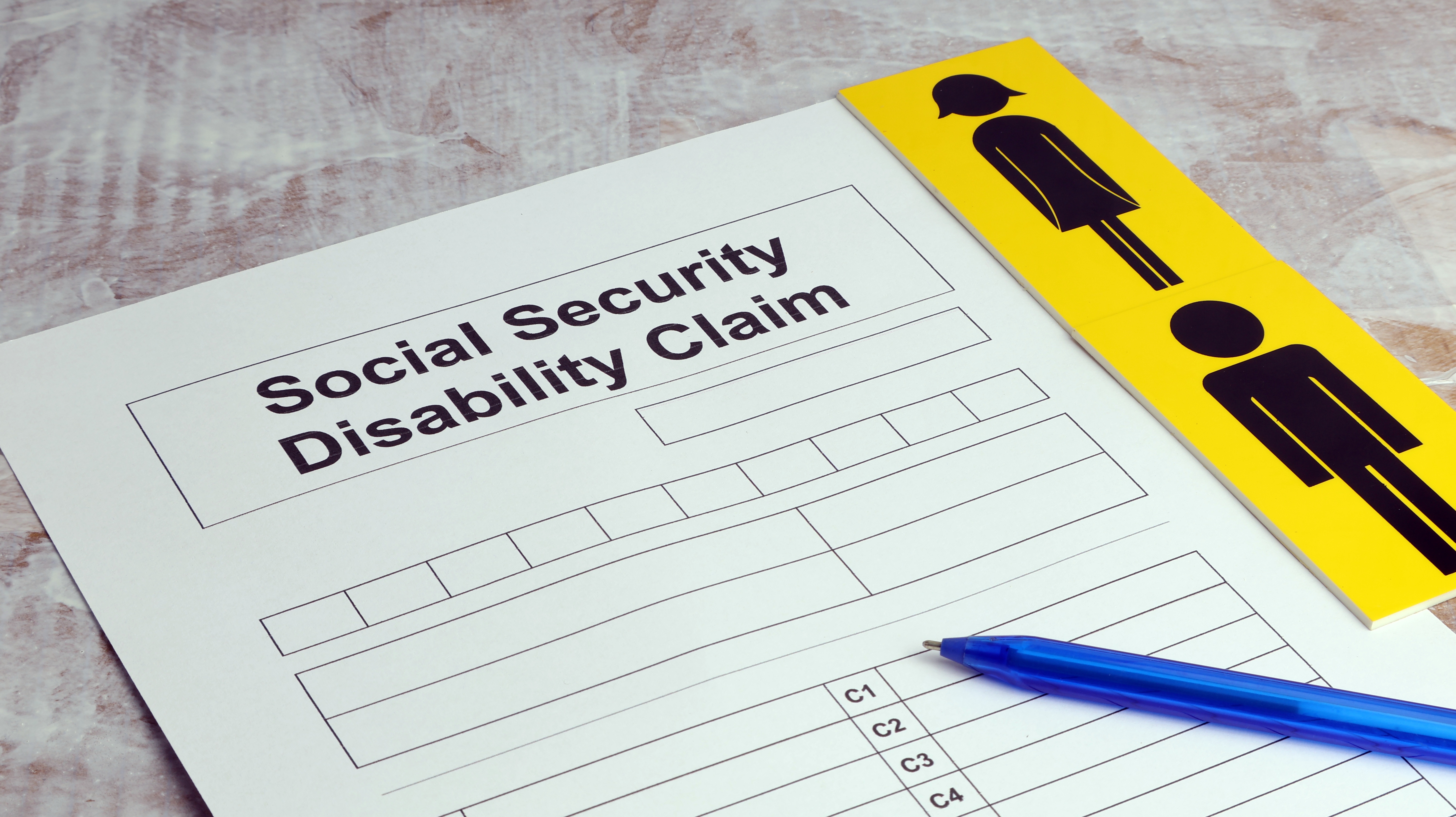 A close-up image of a Social Security Disability Claim form on a desk, accompanied by a blue pen and a yellow card with male and female restroom icons.