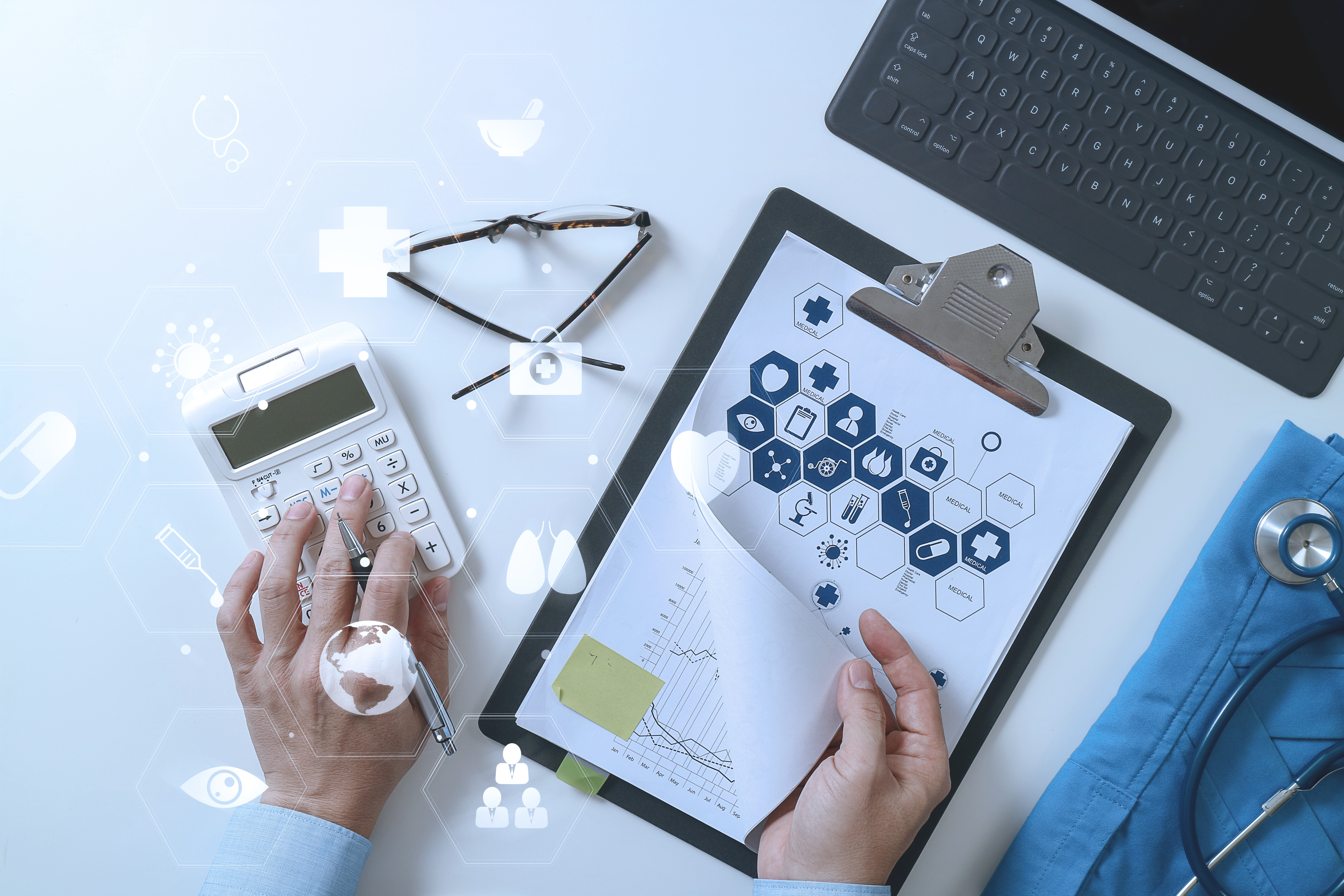 A professional calculating finances with a white calculator and reviewing documents on a clipboard featuring medical icons, surrounded by a stethoscope, glasses, and a keyboard, representing equipment financing for healthcare.