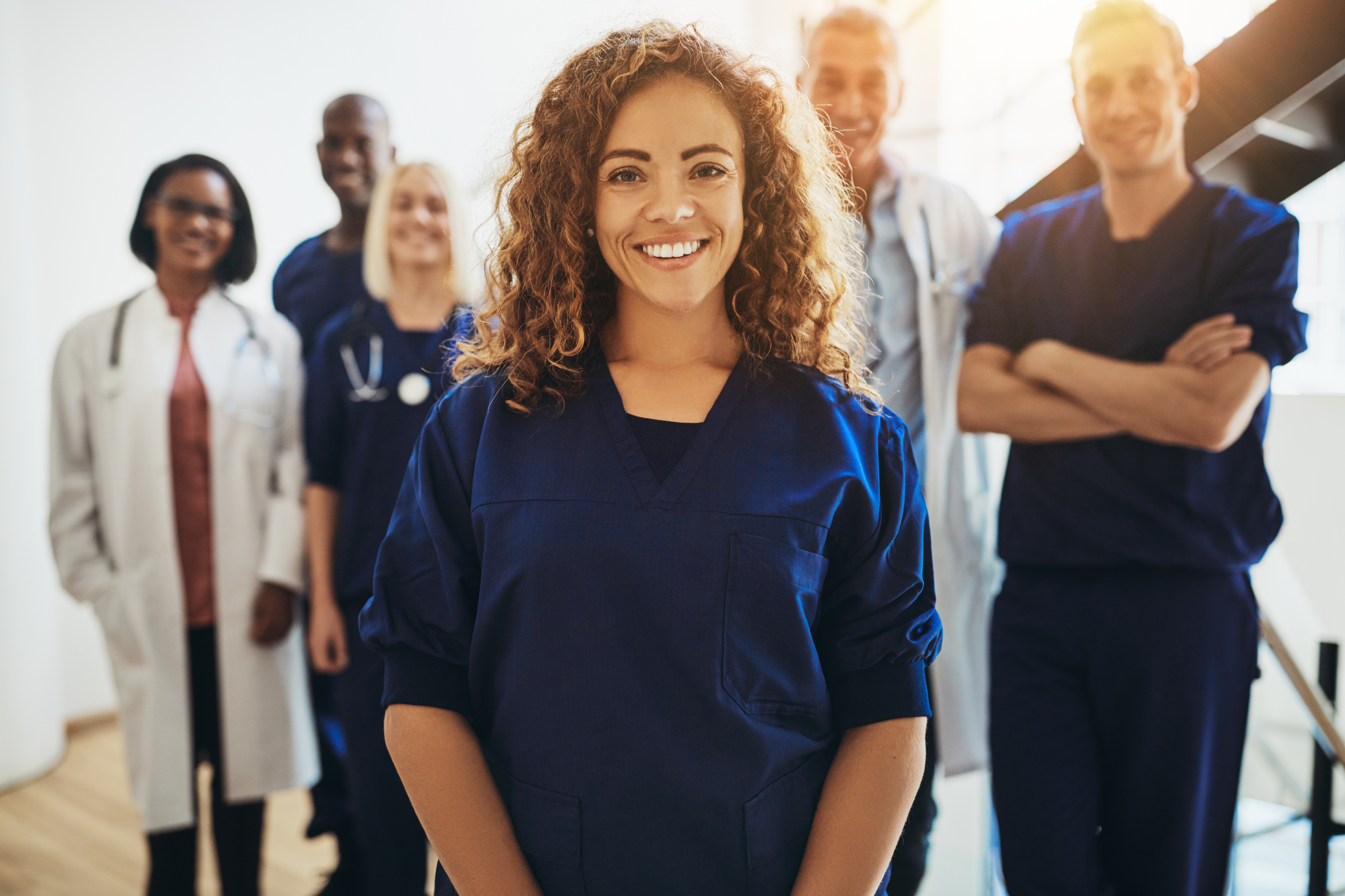 A group of medics standing in a line and smiling. they wear navy blue and white uniforms, and the sunlight illuminates them.