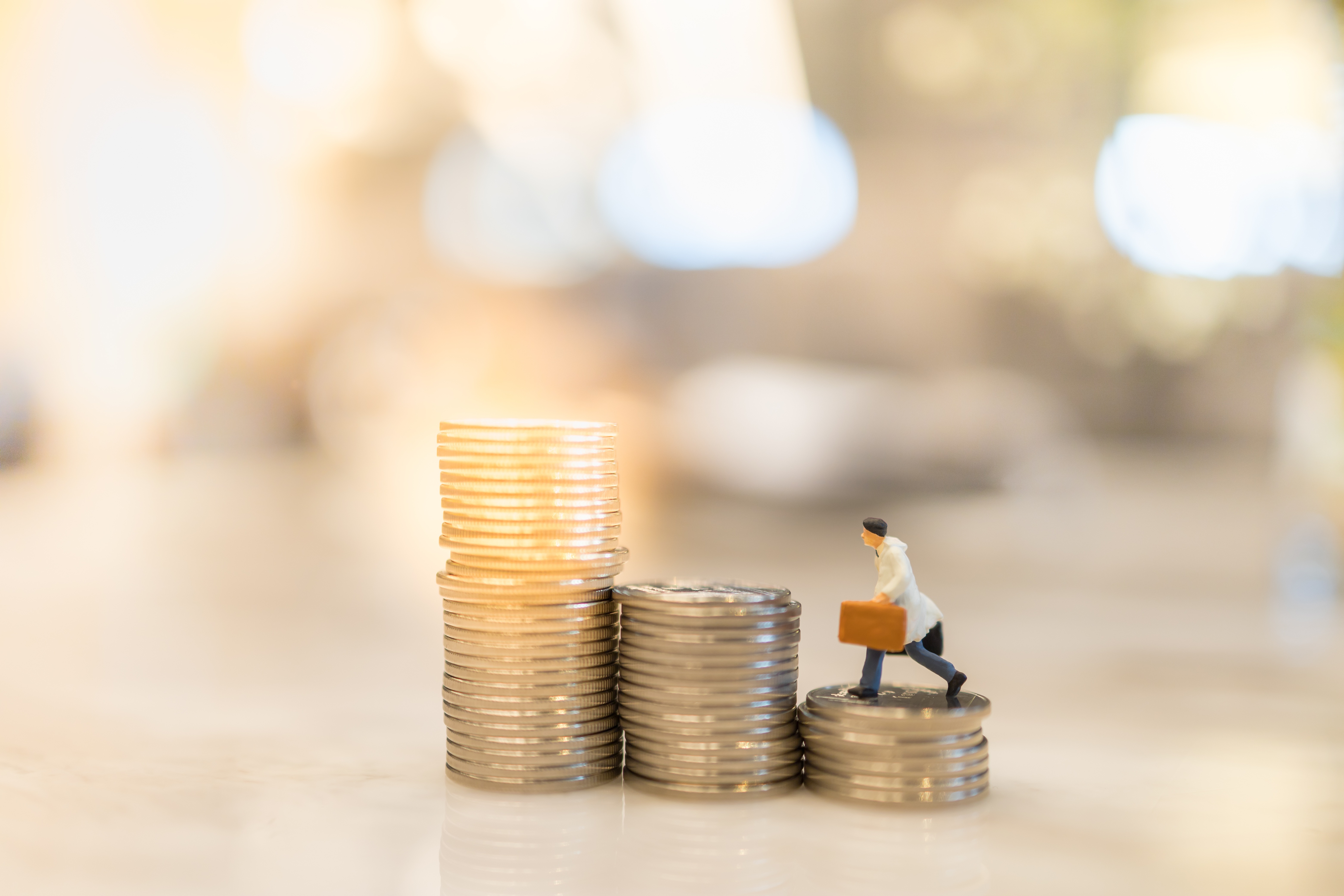  A miniature figurine of a person carrying a briefcase, walking up stacks of coins, symbolizing financial growth and career progression.