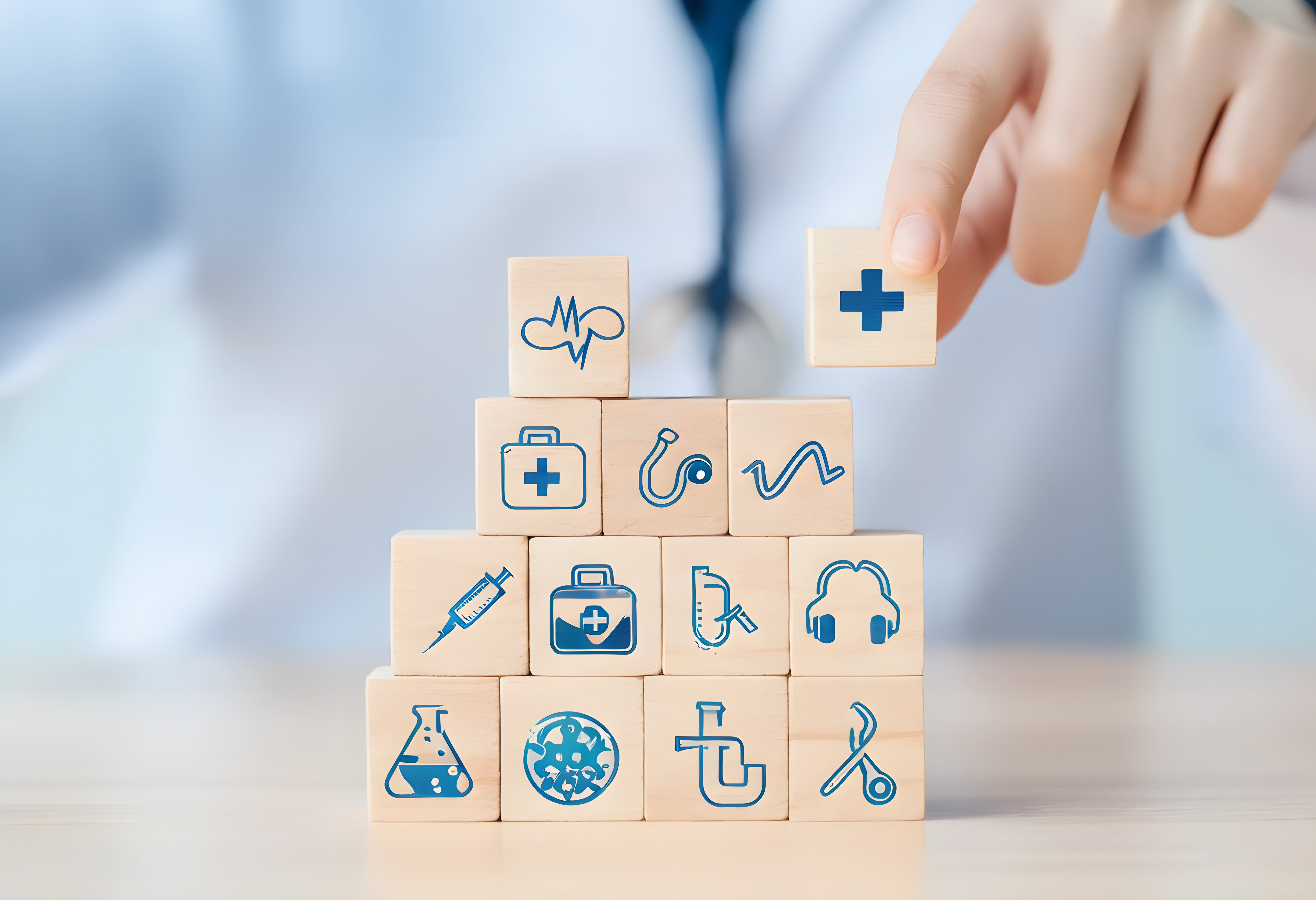 A hand stacking wooden blocks with blue healthcare icons, including a cross, stethoscope, and syringe, symbolizing medical concepts like Types of insurance for doctors.